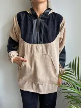 Canguro de pana color beige con capucha, mangas largas de cuero sintético negro y cierre frontal parcial con cremallera.