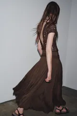 Vestido largo color marrón con detalle de crochet en el corpiño, escote redondo y manga corta. Cierre en la espalda con lazadas.