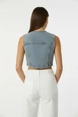 Chaleco corto de jean celeste lavado, con escote en V, botones frontales y bolsillos superiores con tapa.