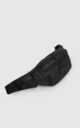 Riñonera negra confeccionada en cordura impermeable de alta resistencia. Presenta tres compartimentos principales con cierres metálicos, un bolsillo lateral adicional y una correa ajustable de alta densidad con broche de seguridad. Incluye una chapa metálica decorativa en el frente.