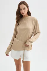 Blusa de poliéster color negro con cuello alto, mangas largas, diseño holgado, detalles de frunces y lazo ajustable en la cintura.