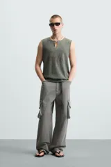 Camiseta sin mangas de punto acanalado, color verde oliva desgastado, con cuello redondo y abertura frontal en forma de 'V'. Presenta un estampado desvanecido en el centro del pecho.