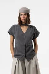 Camisa gris de corte relajado, con escote en V y lazo largo incorporado en el cuello. Mangas cortas con vuelta y frunce sutil en los hombros.