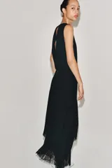 Vestido midi de Zara Woman Collection color negro, sin mangas, con cuello redondo y espalda abierta. Presenta un diseño asimétrico en el bajo adornado con flecos a tono, y cierre trasero con cremallera y botón.