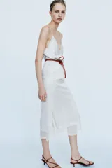 Falda midi de tiro medio, color blanco, confeccionada en hilatura de viscosa 100%, con detalle de aplicación de tejido combinado semitransparente con abertura en el bajo y cierre lateral con cremallera oculta.