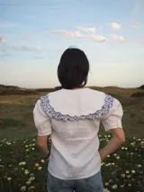 Blusa blanca de lino, de manga corta, con cuello marinero amplio decorado con estampado azul.