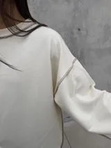 Buzo oversize de color crudo con diseño de costuras expuestas en contraste y terminaciones desflecadas en mangas y ruedo. Presenta un corte holgado con mangas anchas.