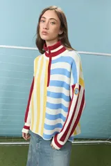 Sweater de punto de algodón con diseño de bloques de rayas verticales y horizontales en colores rojo, amarillo, azul y blanco. Presenta cuello alto con cierre frontal parcial y mangas largas con puños acanalados.