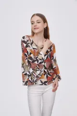 Blusa estampada con flores en tonos marrones, naranjas y negros, con mangas 3/4 acampanadas y cuello redondo.