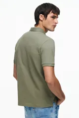Remera polo H&M de manga corta en piqué de algodón, color verde militar, con cuello camisero y tapeta frontal de dos botones. Corte estándar para una silueta clásica y cómoda.