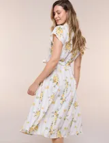 Vestido camisero midi de silueta evasé, confeccionado en tejido liviano blanco con estampado floral amarillo y rayas celestes. Cuenta con cuello solapa en V, cartera con botones frontales, mangas cortas japonesas y cintura definida con lazo ajustable a juego.
