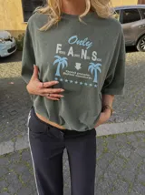 Remera oversize marrón con estampado gráfico frontal en tonos celestes y blancos con la leyenda "Only Fans", palmeras y estrellas.