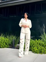 Pantalón blanco roto de corte recto con detalles de calados florales en las piernas.