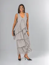 Vestido largo de seda italiana color gris, sin mangas, con escote en V decorado con detalles de paillettes. Presenta diseño de múltiples capas con volados escalonados y bordes deshilachados.