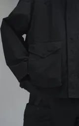 Campera técnica liviana de microfibra negra con acabado mate, capucha ajustable, cierre frontal oculto bajo solapa, bolsillos frontales con solapa y cordón ajustable en la cintura.