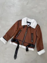 Campera estilo aviador en color camel, confeccionada en gamuza sintética con interior y cuello de piel sintética blanca. Presenta detalles en cuero sintético negro, cierre frontal, bolsillos laterales con cierre y cinturón ajustable en la cintura.
