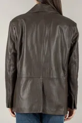 Chaqueta tipo blazer oversize de cuero sintético negro, con solapas de muesca, cierre frontal de dos botones y dos bolsillos de parche frontales.