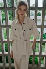 Chaqueta de estilo safari confeccionada en mezcla de lino, color azul marino, con cuello solapa, mangas cortas y cierre frontal con botones ocultos. Presenta bolsillos de parche en el pecho con solapa y botones, además de un cinturón ajustable del mismo tejido para anudar en la cintura.