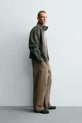 Pantalón de corte baggy fit confeccionado en tejido de algodón con estructura diagonal y efecto lavado. Presenta cintura con pliegues frontales, bolsillos laterales, bolsillos traseros de vivo y un bolsillo lateral adicional con doble vivo en la pernera. Cierre frontal con cremallera y botón.