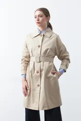Trench de diseño clásico en color beige, con cierre frontal de botones, cinturón ajustable con hebilla a tono y mangas con trabillas en los puños.