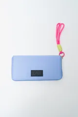 Billetera rectangular con cierre, color celeste pálido, con parche frontal negro que lleva las letras "CNJ" en relieve. Incluye un llavero de muñequera con cordón trenzado en rosa fuerte y verde lima.