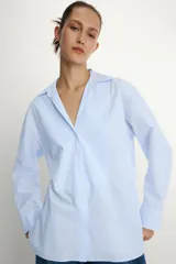 Camisa de popelín confeccionada en algodón, con cuello solapa, escote en pico y cierre frontal con botones. Presenta mangas largas con puños y un bajo redondeado asimétrico.