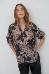 Camisa de corte recto con estampado floral en tonos beige y negro, cuello mao con escote en V y cierre frontal parcial con botones. Presenta mangas tres cuartos con detalle de trabilla para ajustar.