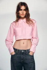 Camisa corta de manga larga con diseño a rayas verticales en tonos rosados. Presenta cuello solapa, cierre frontal con botones ocultos y dos bolsillos delanteros de plastrón.