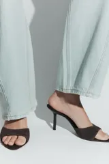 Sandalia tipo mule de tacón fino alto, confeccionada en serraje de color marrón con tira delantera ancha y punta redonda.