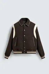 Cazadora estilo varsity de corte cropped, confeccionada en tejido de lana marrón con mangas en contraste color crema. Presenta cuello solapa, cierre frontal con botones a presión, bolsillos laterales de vivo y acabados en rib a rayas en puños y cintura.