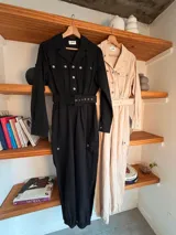 Mono de gabardina negro con cuello camisero, cierre frontal con botones metálicos, mangas largas y bolsillos tipo cargo en el pecho y las piernas. Incluye un cinturón ancho con hebilla del mismo tono para ajustar la cintura.