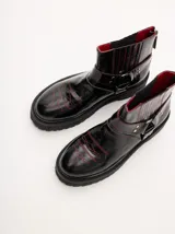 Bota corta de cuero negro tipo biker, con suela track de goma, plataforma, costuras y bordados decorativos en hilo rojo. Presenta tiras con hebillas metálicas y cierre en la parte trasera.