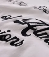 Camisa boxy color crema de algodón texturizado, con cuello inglés, mangas cortas, bolsillos delanteros y lettering bordado.