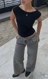 Pantalón de jean estilo wide leg, de tiro bajo, color gris lavado con efecto desgastado. Presenta corte recto y holgado en las piernas, con cierre frontal y bolsillos clásicos.