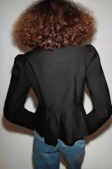 Chaqueta negra de cuello redondo, manga larga con hombreras abullonadas y cierre frontal con ganchos metálicos.