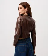 Campera de cuero sintético color marrón, con cuello redondo, cierre frontal y bolsillos laterales con cremallera. Presenta costuras verticales decorativas que le dan un diseño estructurado.