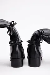 Bota bucanera de cuero vacuno color negro, con caña alta y detalle de lazos decorativos en la parte posterior. Cuenta con taco bajo cuadrado y punta redondeada.