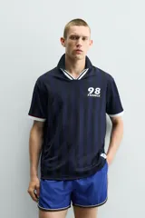 Polo de corte relajado confeccionado en tejido técnico, con diseño de rayas verticales en tonos azul marino y negro. Presenta cuello solapa con abertura frontal y detalles de rib en contraste en cuello y mangas. Incluye estampado frontal con el número 98 y la inscripción France, además de una etiqueta aplicada en el ruedo inferior.