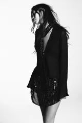 Camisa semitransparente negra de viscosa, con escote en pico pronunciado y manga larga con volantes. Incluye un foulard del mismo tejido con bordados florales y abalorios a contraste en tonos dorados y plateados.