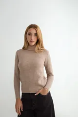Buzo de punto color beige con cuello alto, manga larga y puños y ruedo acanalados.