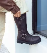 Bota de caña alta confeccionada en cuero vacuno encerado, con diseño de estilo biker. Presenta detalles de hebillas metálicas niqueladas en la caña y cierre lateral. Cuenta con suela de cuero artesanal y forrería vacuna en su interior.