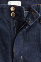 Pantalón de jean de denim oscuro, tiro alto, con pierna ancha y corte recto desde la cadera hasta el bajo. Presenta pliegues frontales y traseros, y un dobladillo ancho en los tobillos. Cierre frontal con dos botones dorados.