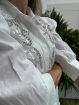 Camisa blanca de mangas 3/4 con bordados de lentejuelas y mostacillas plateadas en el frente.