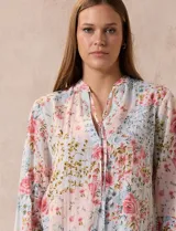 Blusa de gasa plisada con estampado floral en tonos rosas y celestes. Presenta cuello a la base con escote en V y lazo de ajuste frontal, mangas largas con puños elásticos y corte recto.
