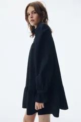 Vestido corto de corte holgado con cuello alto de volados y cierre frontal de botón. Presenta canesú fruncido, mangas largas abullonadas con puños acampanados y falda con costura fruncida en el bajo.