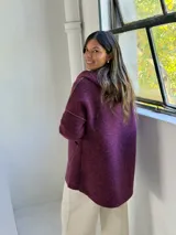Tapado de paño color magenta con capucha integrada, cierre frontal y bolsillos laterales. Presenta detalles en color beige en el interior de la capucha, puños y bordes de los bolsillos.