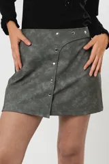 Minifalda gris con textura símil cuero, corte irregular con sobrefalda y cierre frontal con broches metálicos.