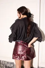 Blusa negra con corte holgado, volados blancos en cuello, mangas y frente, y ajuste en los puños.