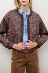 Chaqueta bomber color bordó con mangas de cuero sintético marrón y cuerpo de tweed con patrón de espiga. Cierre frontal con botones a presión y cuello redondo.