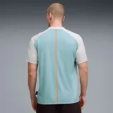 Camiseta deportiva PUMA de McLaren Racing, con diseño en celeste y blanco, cuello en V y detalles en naranja. Presenta el logo de PUMA, el emblema de la escudería y el patrocinio principal en el frente.